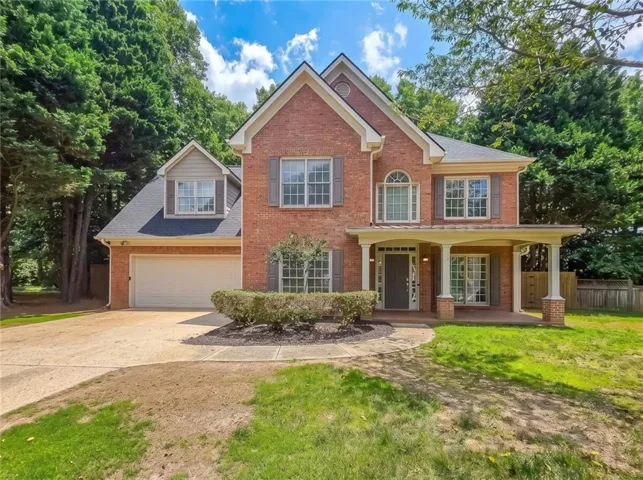 Traditional brick exterior featuring a covered front porch, arched window accents, a two-car garage, and mature landscaping