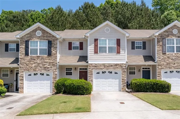 Townhome exterior featuring stone veneer accents, neutral siding, contrasting shutters, individual garage doors, and front entryways