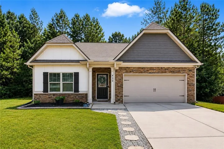 Exterior featuring a stone facade, gabled roof, two-car garage, concrete driveway, and front lawn