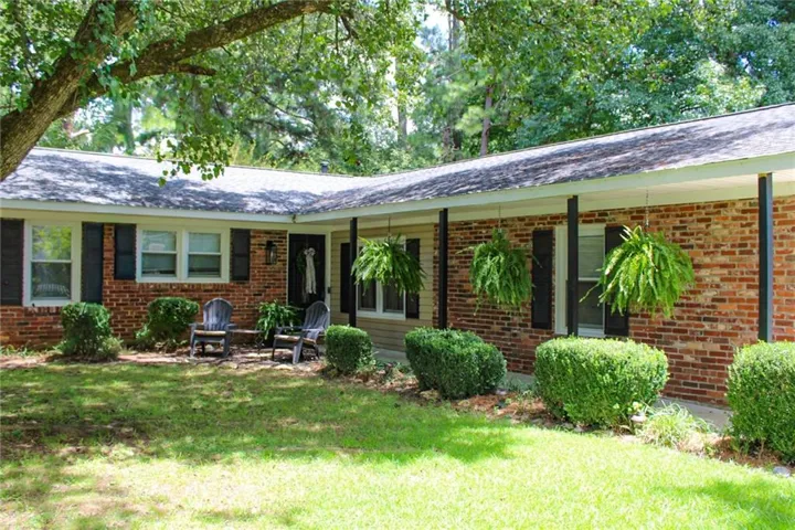Brick exterior with a covered front porch, featuring dark shutters, established landscaping, and a manicured lawn