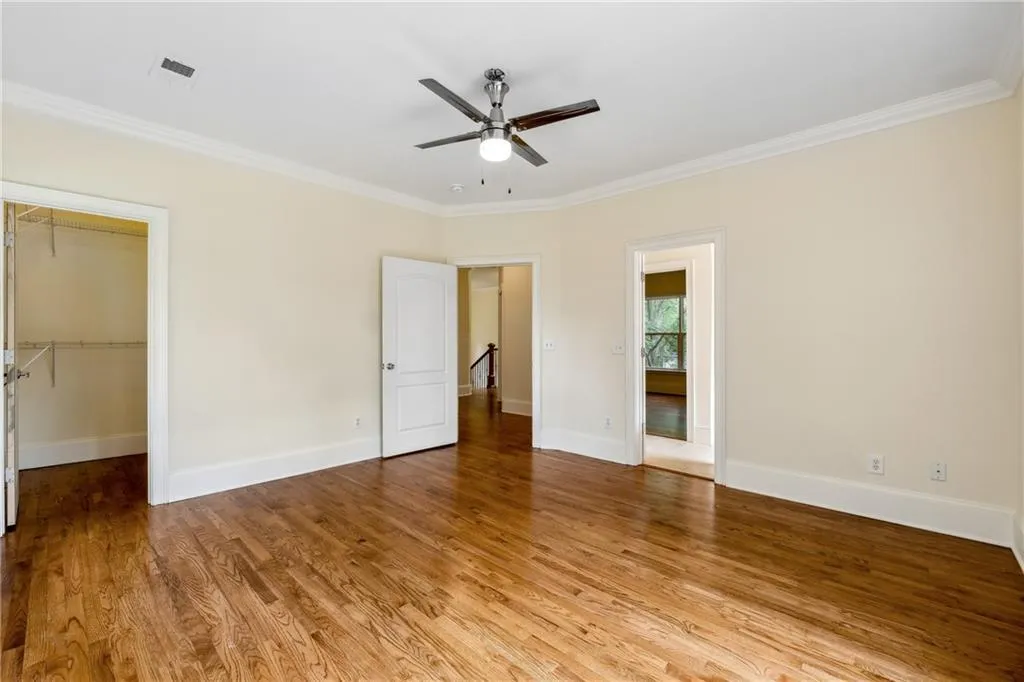 Unfurnished bedroom featuring a spacious closet, a closet, ceiling fan, ornamental molding, and light hardwood / wood-style floors
