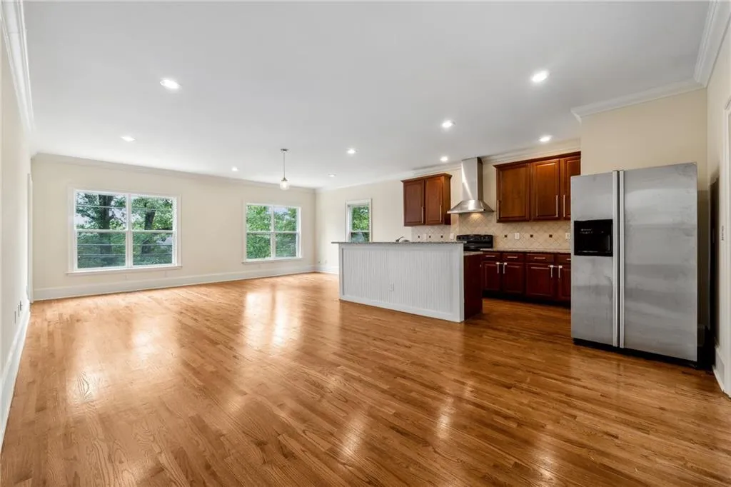 Kitchen featuring wall chimney range hood, decorative backsplash, hardwood / wood-style flooring, stainless steel fridge, and a center island with sink