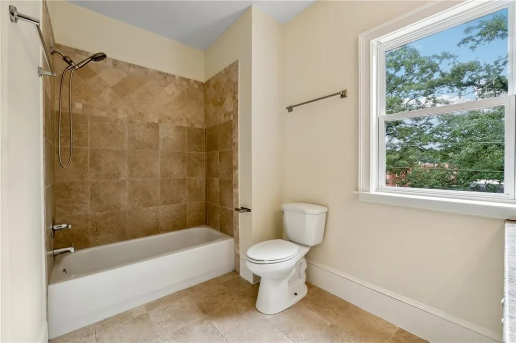 Bathroom featuring a healthy amount of sunlight, tiled shower / bath, tile patterned floors, and toilet