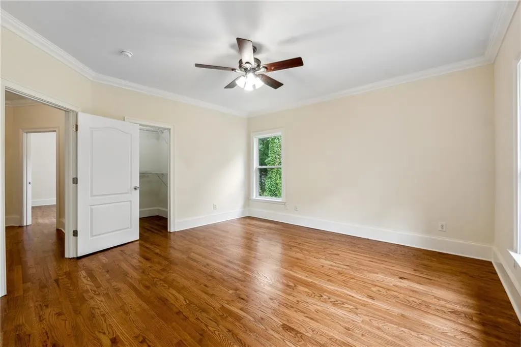 Unfurnished bedroom with a spacious closet, crown molding, ceiling fan, and hardwood / wood-style floors