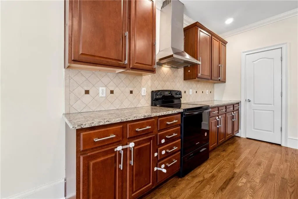 Kitchen with wood-type flooring, tasteful backsplash, wall chimney exhaust hood, black electric range oven, and ornamental molding
