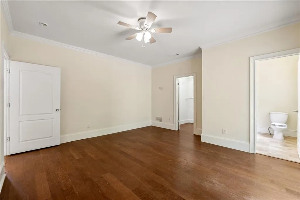 Unfurnished bedroom featuring ornamental molding, connected bathroom, hardwood / wood-style flooring, and ceiling fan
