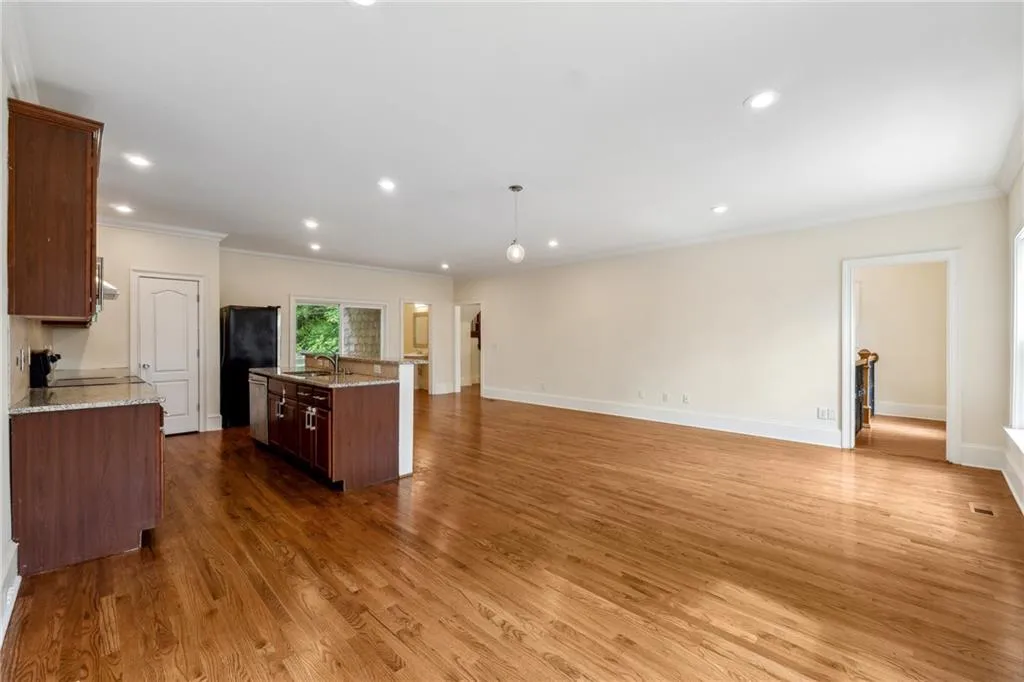 Kitchen with a center island with sink, hardwood / wood-style floors, sink, hanging light fixtures, and light stone countertops