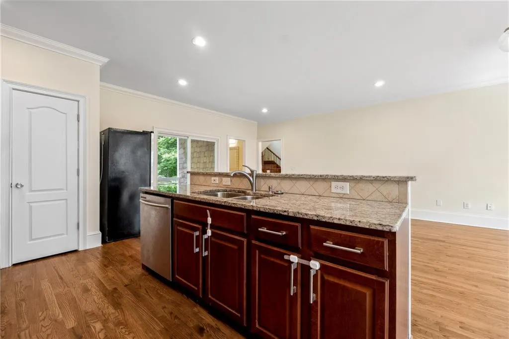 Kitchen featuring dishwasher, a kitchen island with sink, black fridge, hardwood / wood-style floors, and sink