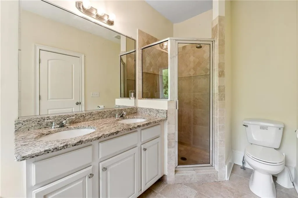 Bathroom featuring a shower with door, double vanity, tile patterned flooring, and toilet