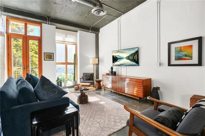 Spacious living area featuring high ceilings, exposed ductwork, large wood-frame windows, wood-finish flooring, and a ceiling fan