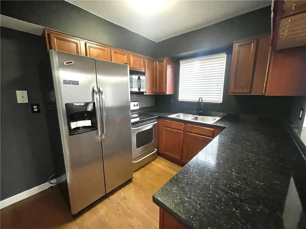 Kitchen featuring stainless steel appliances, sink, dark stone counters, and light hardwood / wood-style flooring