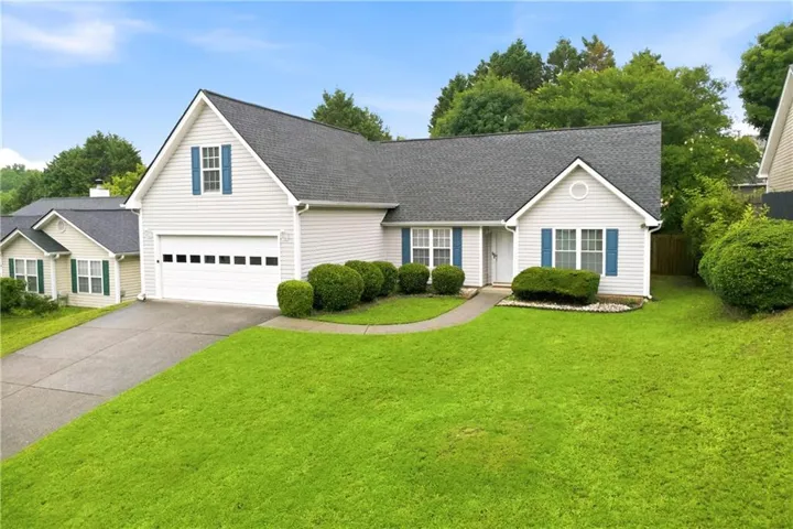 Single-story residence featuring light-colored siding, a dark shingle roof, a two-car garage with a panel door, blue window shutters, and a concrete driveway