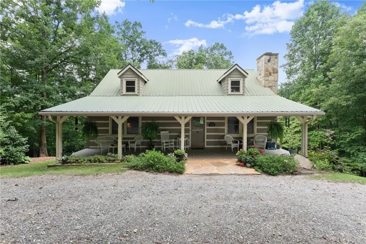 Log cabin exterior featuring a green metal roof, a stone chimney, and a full-length covered porch with exposed beams