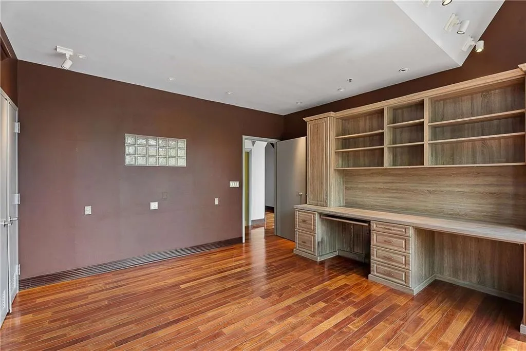 Unfurnished office with built in study area, dark wood-style floors, and arched walkways