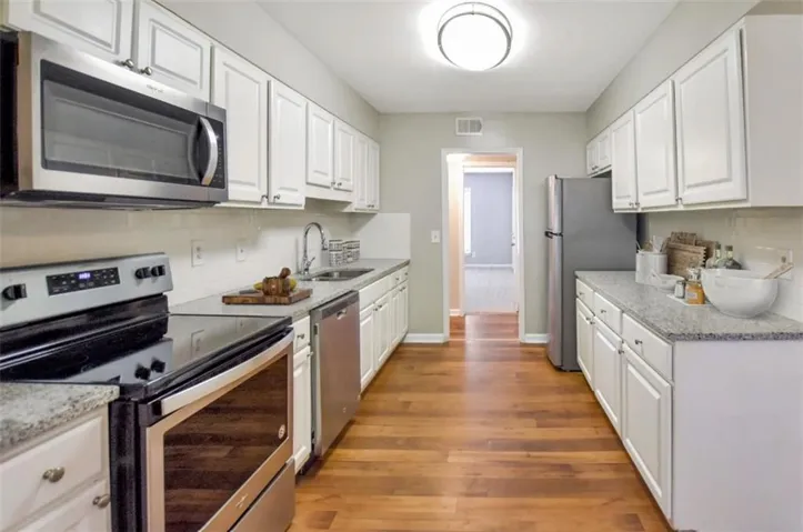 Galley kitchen featuring wood-finish flooring, white cabinetry, speckled countertops, and stainless steel appliances