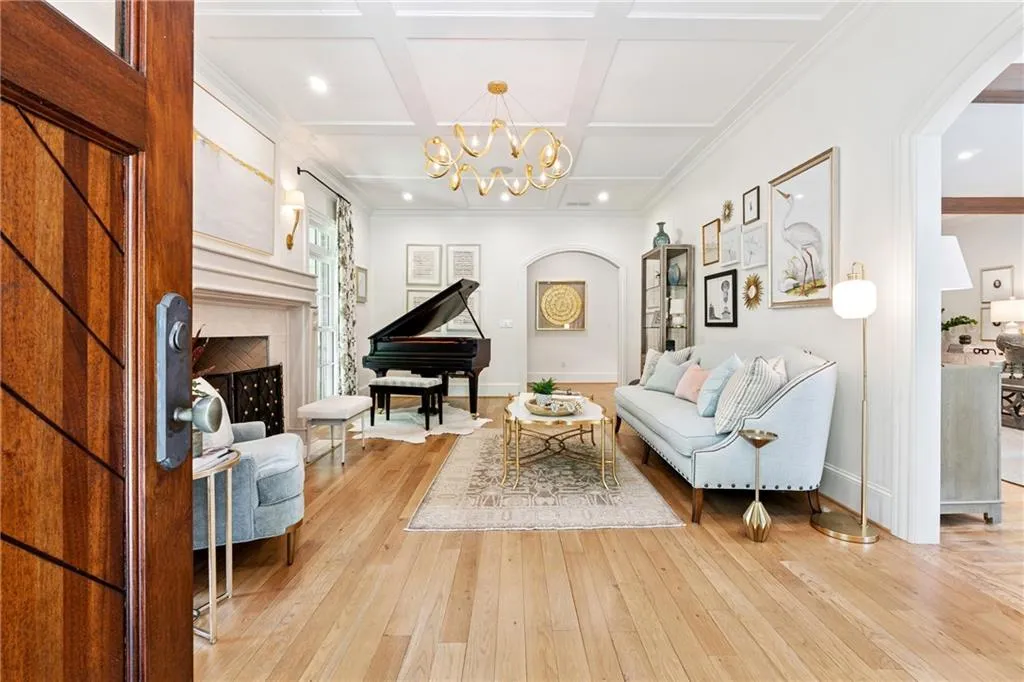 Living room with arched entryways, hardwood flooring, coffered ceiling, a chandelier, and a gas fireplace