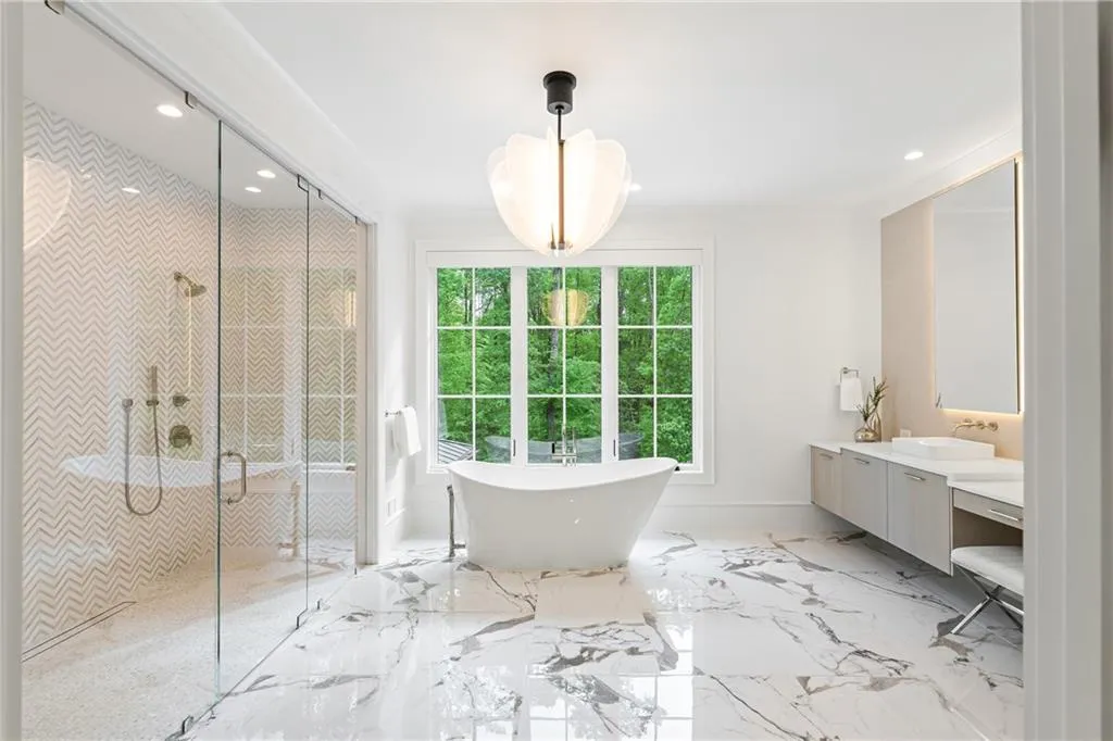 Sunlit primary bath showcases a double shower, soaking tub and vanities adorned with beautiful marble and lighting
