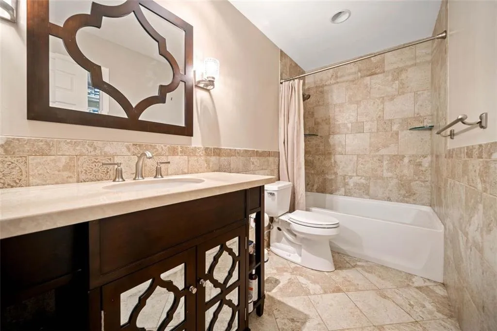 Full bathroom with shower / tub combo with curtain, vanity, tile walls, and toilet