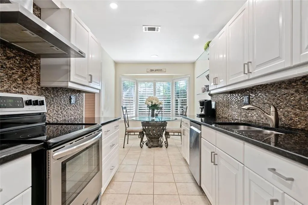 Kitchen with wall chimney exhaust hood, white cabinets, appliances with stainless steel finishes, and sink