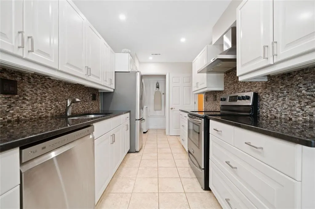 Kitchen featuring stainless steel appliances, white cabinets, sink, wall chimney range hood, and light tile patterned floors