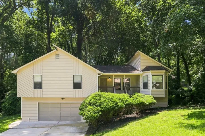 Split-level residence featuring light-toned siding, a two-car garage, and a covered front porch with dark railings