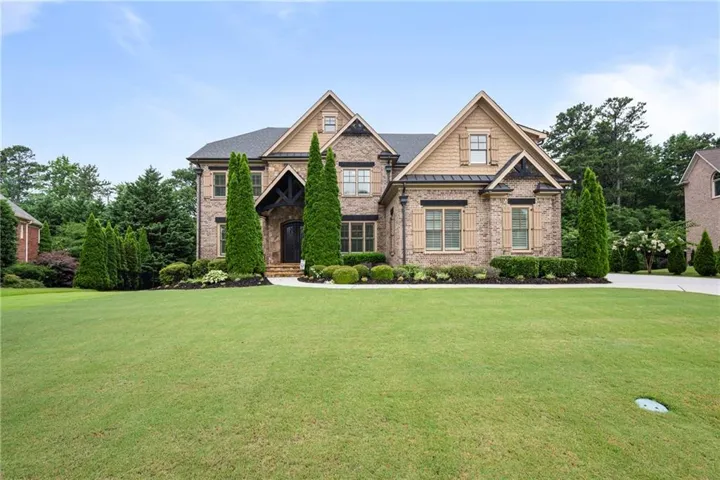 Stately brick and shingle exterior featuring multiple gables, an arched entry with exposed wood beams, decorative window shutters, and a well-maintained front lawn with mature landscaping