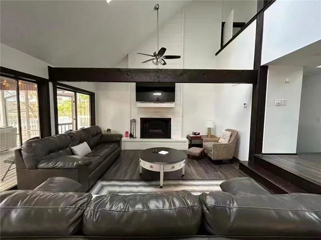 1189 Iris Lake - Vaulted ceiling living area featuring dark wood-finish flooring, exposed dark wood beams, a white shiplap accent wall, and a fireplace with a white mantel