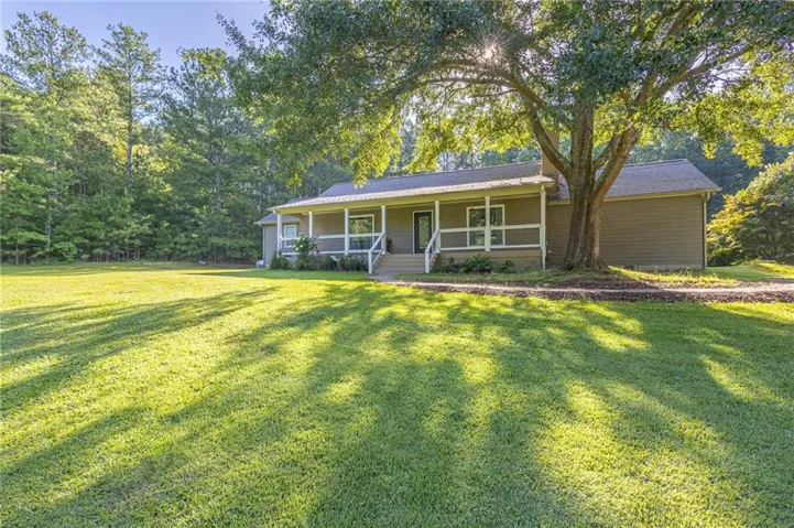 Expansive front lawn with mature trees and a long covered porch with white railings