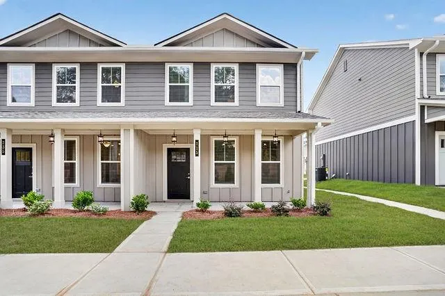 Modern two-story townhomes featuring gray and cream siding, covered front porches with white columns, and black front doors with clear glass inserts