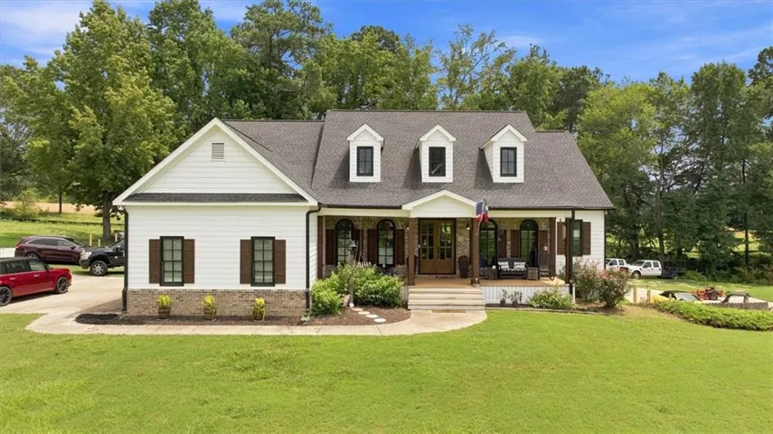 White siding exterior with black shutters, dark shingle roof, front porch with wood columns, and dormer windows