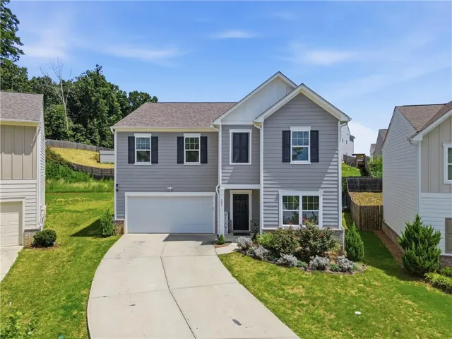 Two-story residence featuring light gray siding, white trim, dark shutters, an attached garage, and a concrete driveway