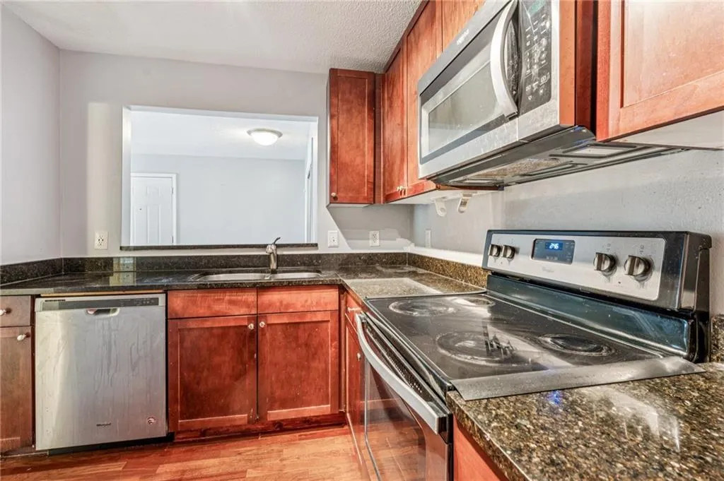 Kitchen with stainless steel appliances, light wood-type flooring, dark stone counters, and a textured ceiling