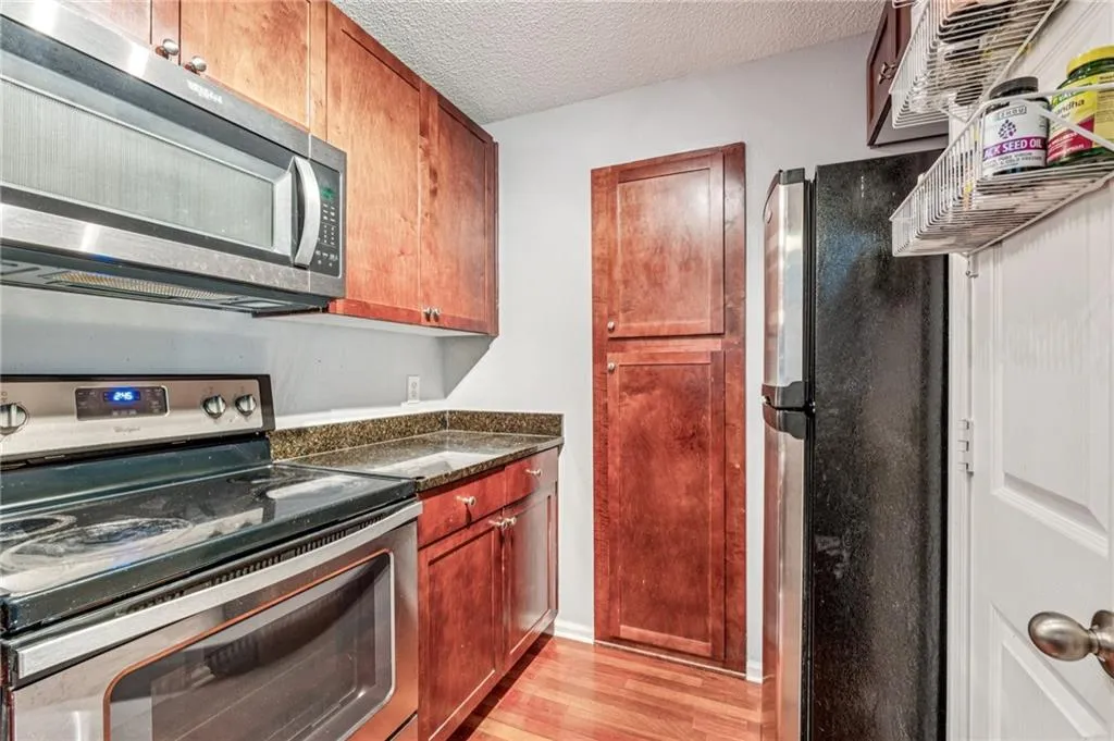 Kitchen with stainless steel appliances, a textured ceiling, light wood finished floors, dark stone counters, and brown cabinets