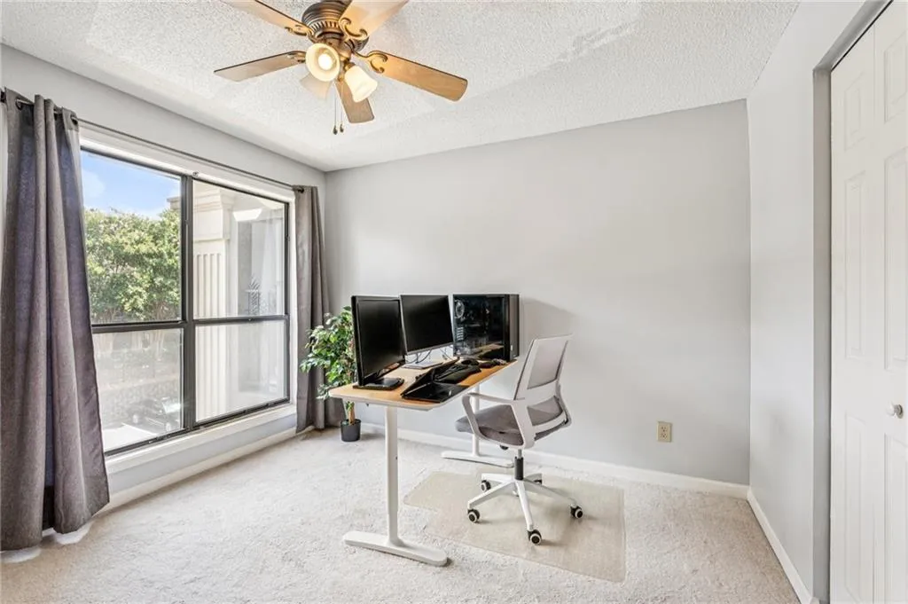 Carpeted office space with a textured ceiling and ceiling fan