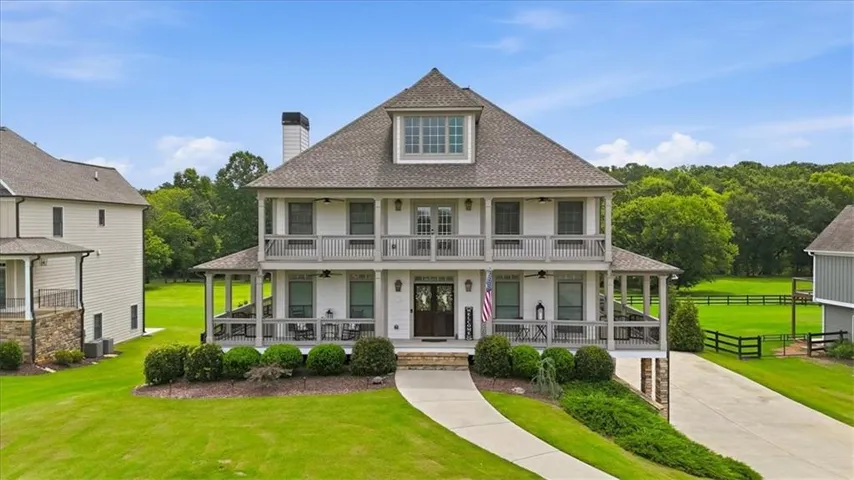 Grand two-story residence featuring a prominent dormer, dual-level covered porches, and a stone-clad foundation
