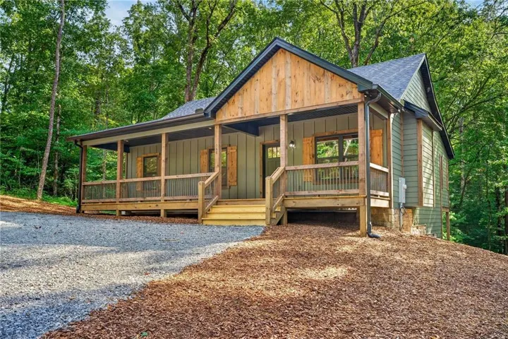Wood-clad gable accent, covered porch with natural wood railings, exterior siding, dark-framed windows with wood shutters, gravel driveway