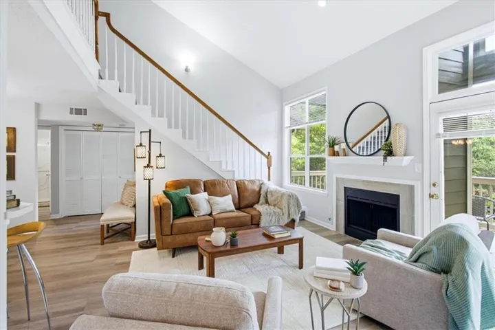 Open-concept living area featuring a vaulted ceiling, wood-finish flooring, and a fireplace with a mantel
