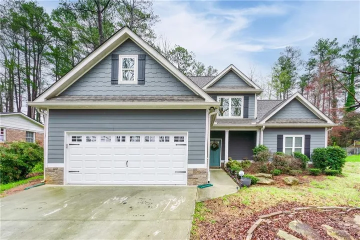 Two-story residence featuring a two-car garage, gray siding, and stone accents