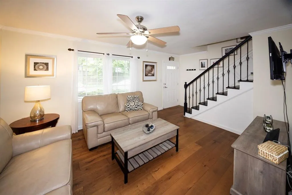 Living room with a ceiling fan, dark wood-style floors, stairway, and ornamental molding