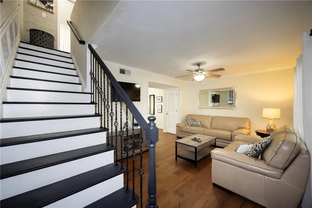 Living area with ceiling fan, dark wood-type flooring, stairway, and ornamental molding
