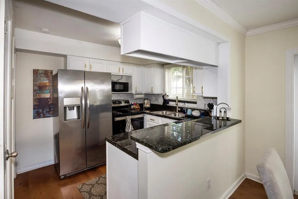 Kitchen featuring stainless steel appliances, dark stone countertops, a peninsula, dark wood-style floors, and ornamental molding