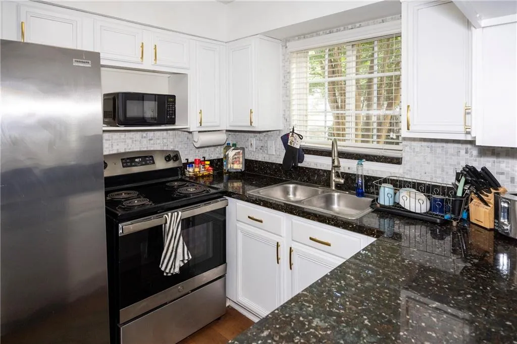 Kitchen featuring stainless steel appliances, white cabinetry, decorative backsplash, and dark stone countertops