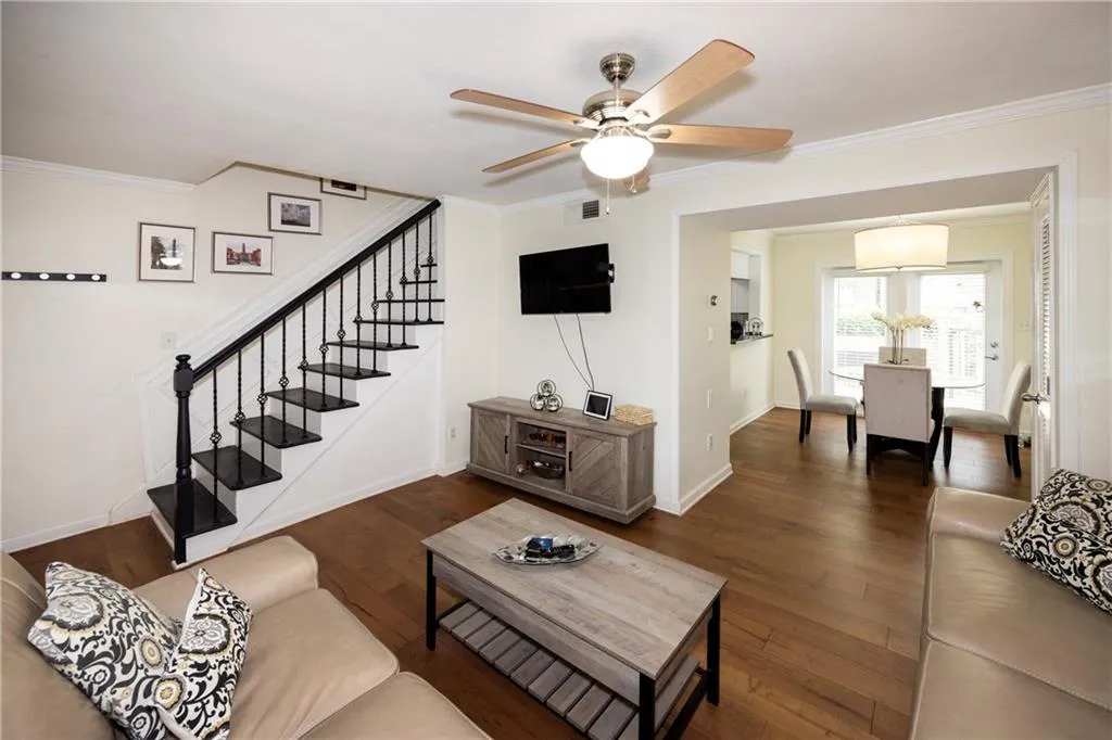 Living area with ornamental molding, ceiling fan, stairs, and dark wood-type flooring