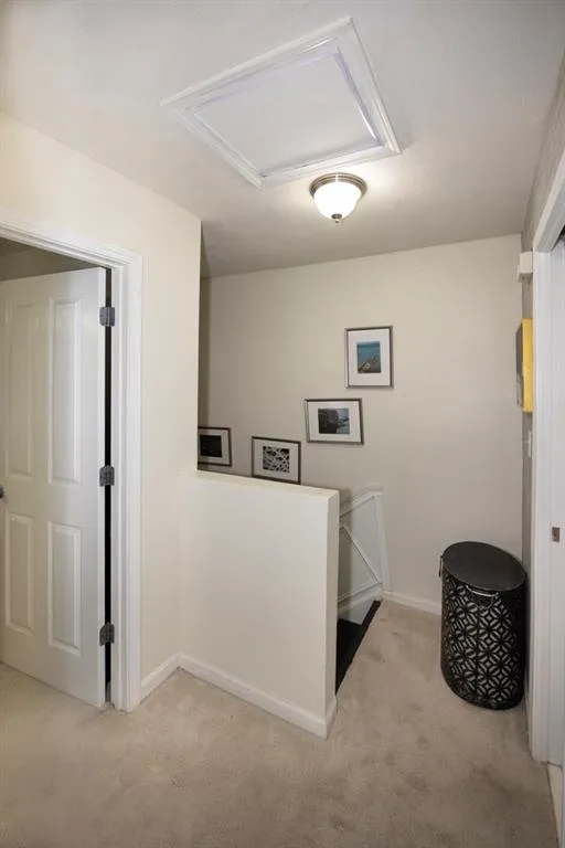 Hall featuring light colored carpet, an upstairs landing, and attic access