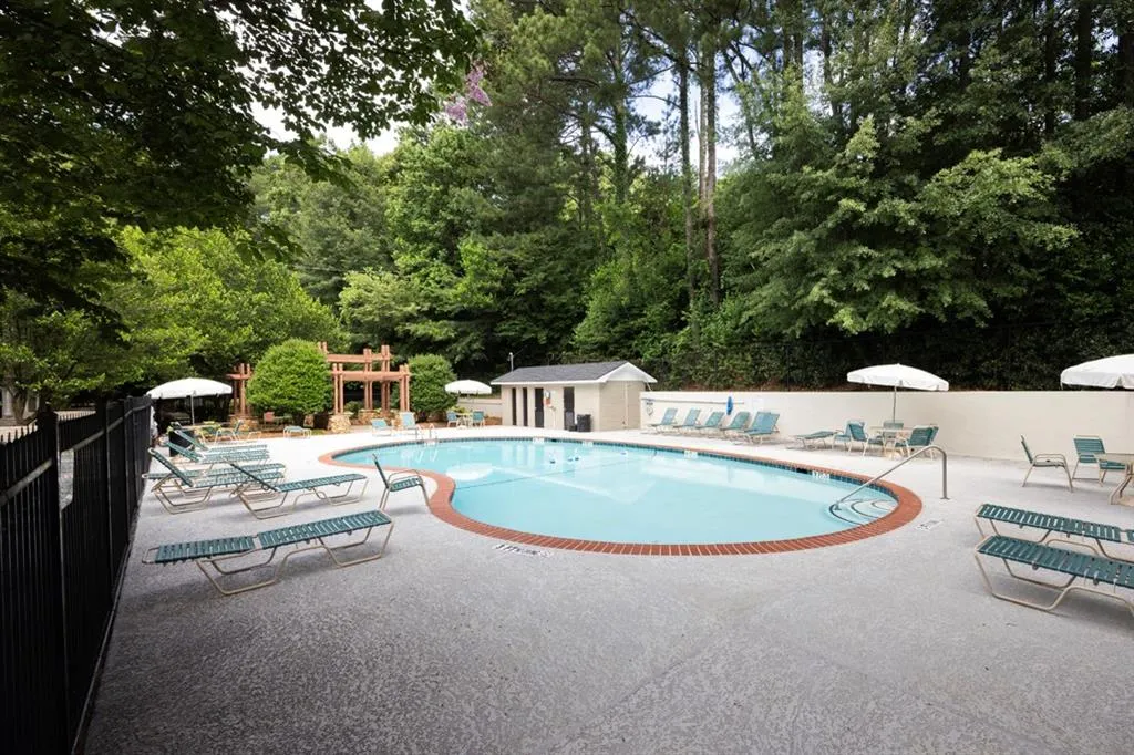 Community pool with a patio, view of scattered trees, and an outbuilding