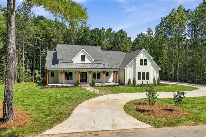 Modern farmhouse exterior with board and batten siding, dark framed windows, a covered front porch with wood columns, and a paved driveway