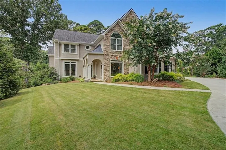 Stately residence featuring a stone and stucco exterior, arched entry, established beautiful landscaping, and cement driveway