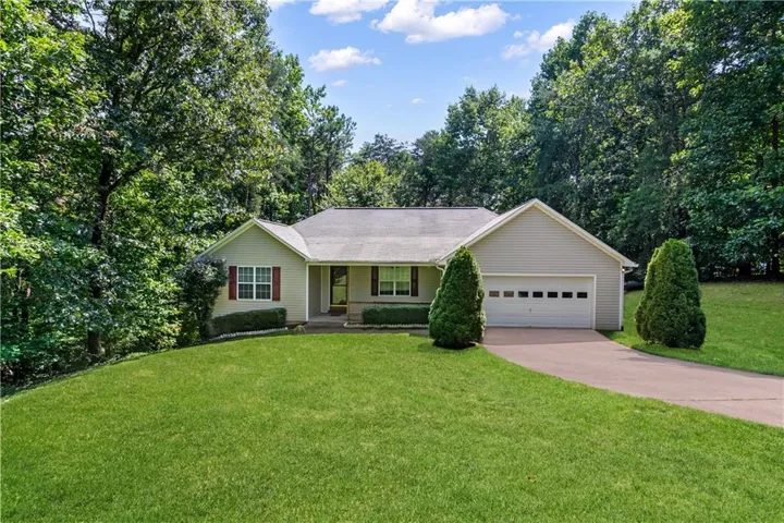 Ranch-style residence featuring a prominent two-car garage, mature landscaping, and a sloped front lawn