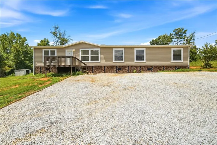 Expansive gravel parking area, wood siding exterior, white-framed windows, and a wood entry deck with stairs