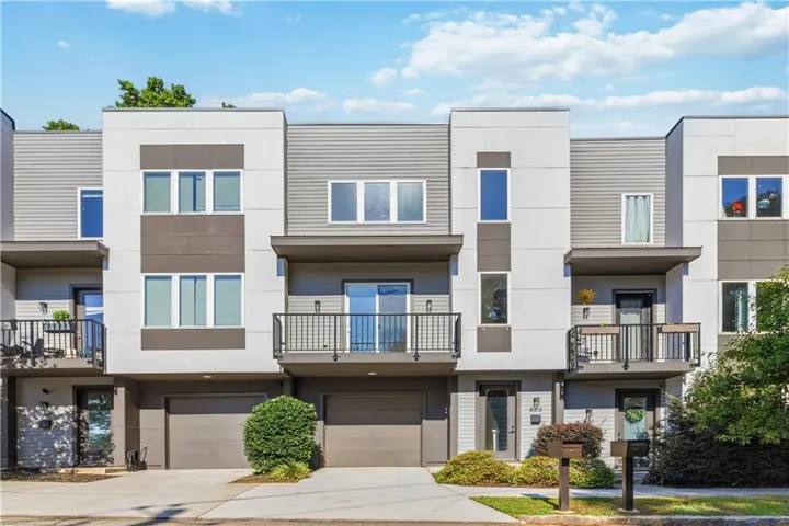 Contemporary townhome exterior featuring multi-toned siding, integrated garage, and a private balcony with black metal railings